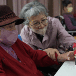 保康基金會＿據點長輩彎腰陪同長照中心長輩，手把手調整花藝作品