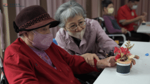 保康基金會＿據點長輩彎腰陪同長照中心長輩，手把手調整花藝作品